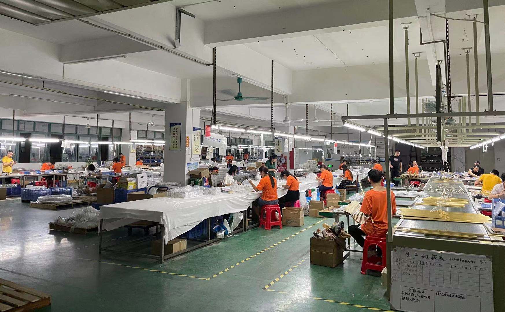 Lighting manufacturing facility with workers in orange uniforms assembling products at long tables in a production line