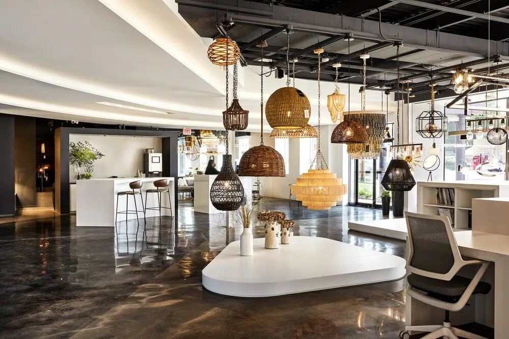 Modern lighting showroom with diverse pendant lights including woven, glass, and metallic fixtures hanging from exposed ceiling, showcasing custom lighting design options