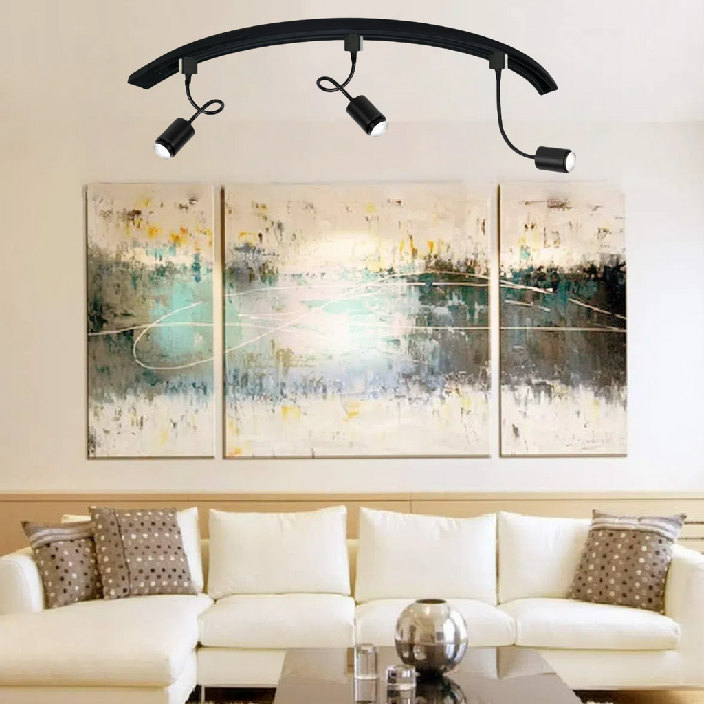 Black arc track lighting with three adjustable spotlights illuminating a living room with white sofa and abstract art