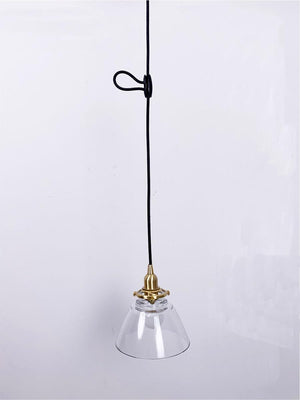 Black cable hook adjuster holding pendant light cord. Clear glass pendant with brass base. Ideal for cord adjustment.