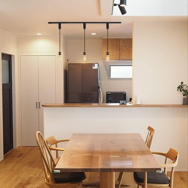 Black industrial track lighting pendants with Edison bulbs above a wooden dining table in a kitchen setting.