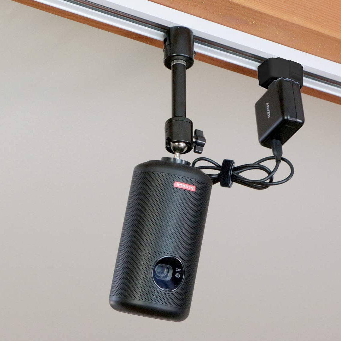 Black projector on ceiling track mount, NEBULA brand, adjustable angle for presentations and home theaters.