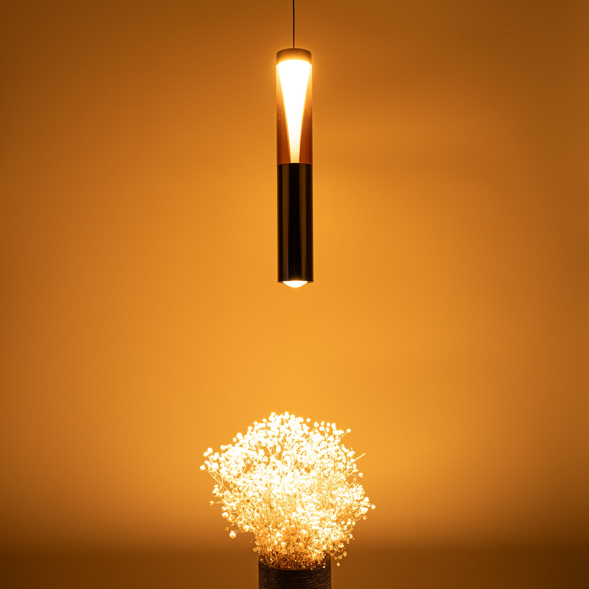 Modern matte black cylinder LED track pendant light casting a warm, cozy glow over a vase of white gypsophila flowers, highlighting the unique ambient crystal prism and focused downward task spotlight effect