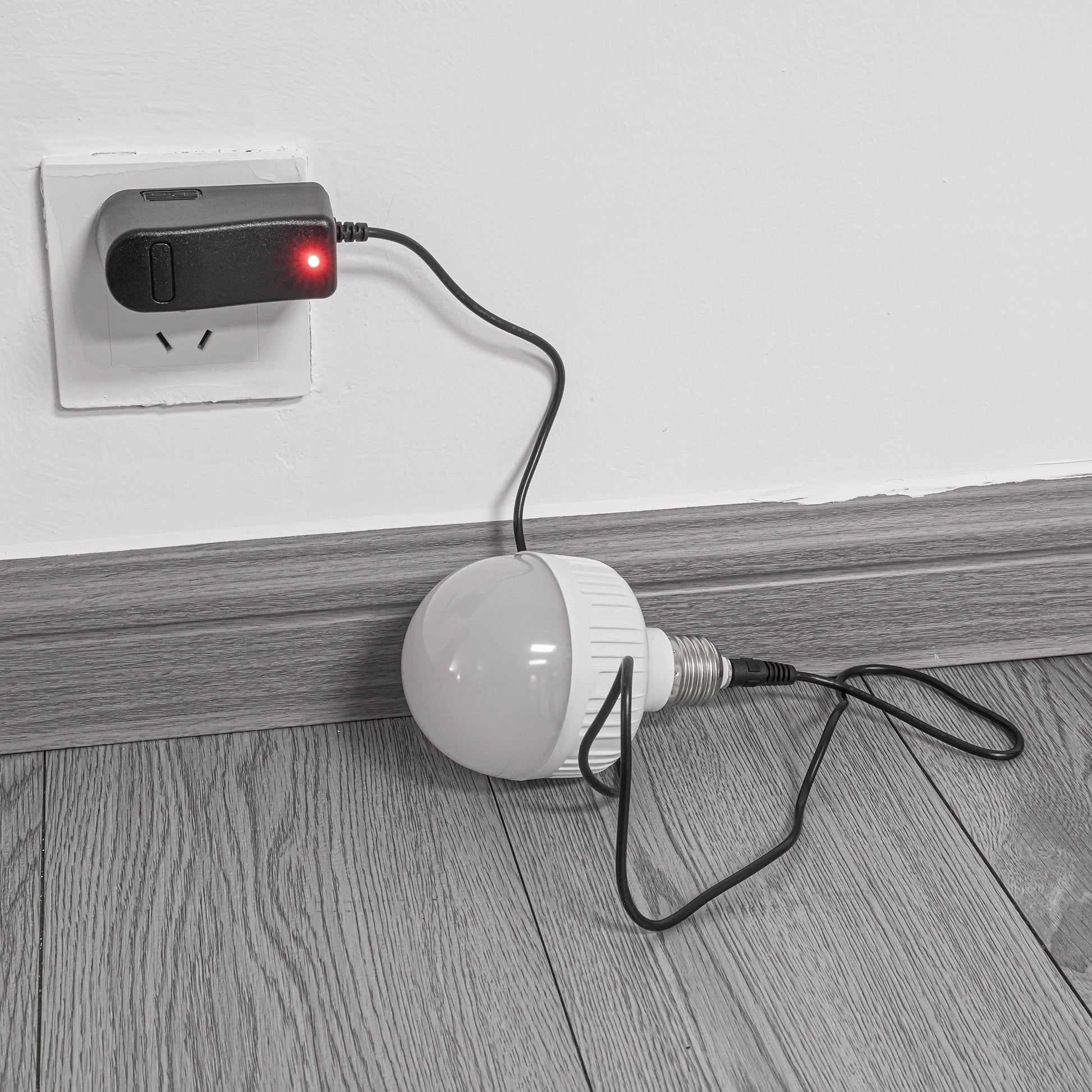 Rechargeable smart LED bulb charging, connected to black charger in wall outlet.