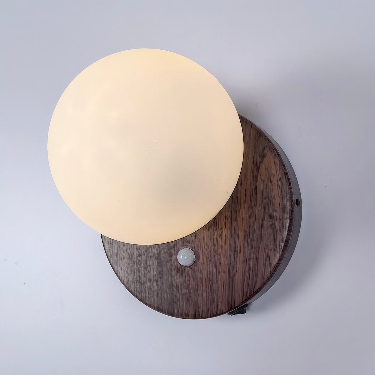 Top view of cordless wall light showing walnut wood base, milk white sphere shade, and motion sensor design
