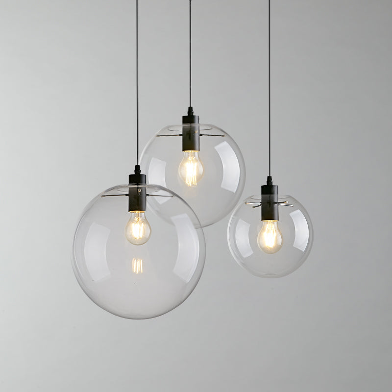 Modern glass globe pendant lights, ideal for sloped ceilings. Black metal hardware, clear glass shades, and E26 base bulbs.