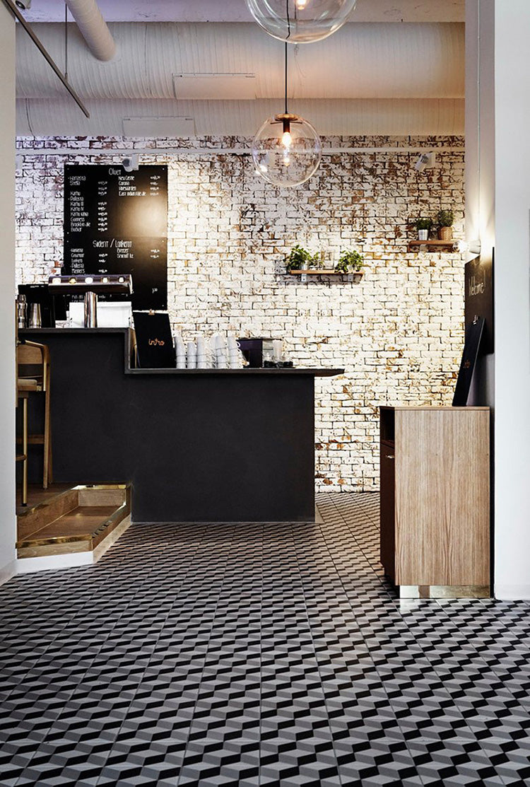 Cafe interior featuring track mount pendant light with glass globe, brick wall, black counter, and stylish patterned floor.