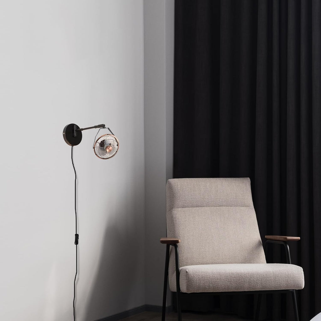 Industrial black wall mount fan with swing arm installed in a modern living room reading corner with accent chair