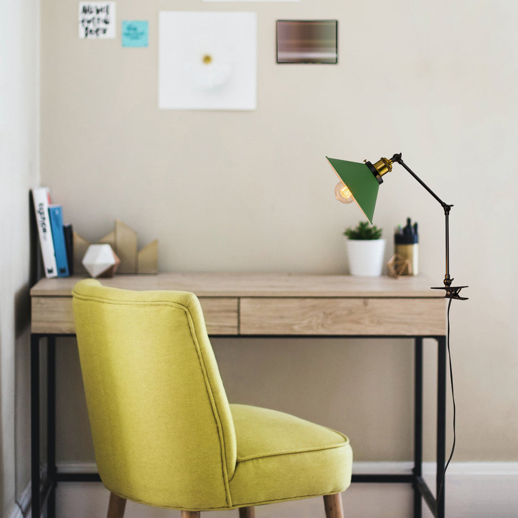 Green clip-on desk lamp on wooden desk with flexible arm. Modern adjustable bedside lamp.